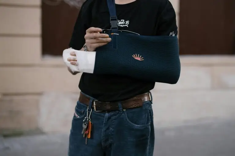 About A man wearing a dark sling with a bandaged arm, standing outdoors in casual attire.